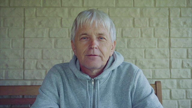 画像中白发苍苍的老人坐在屋外的长凳上视频下载