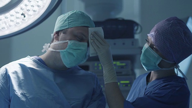 现代手术室中护士擦拭医生前额汗水视频素材