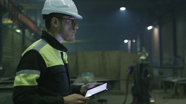 戴安全帽的工程师正带着一台平板电脑穿过一家重工业工厂。视频素材
