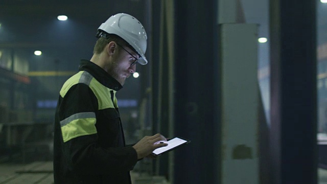 戴安全帽的工程师正带着一台平板电脑穿过一家重工业工厂。是用握手来问候一个工人。视频素材