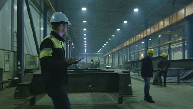 戴安全帽的工程师正带着一台平板电脑穿过一家重工业工厂。视频素材
