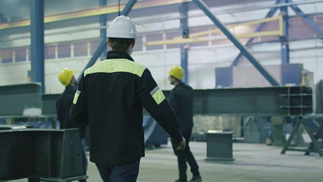 在一家重工业工厂，工程师戴着安全帽与工人们握手致意。视频素材