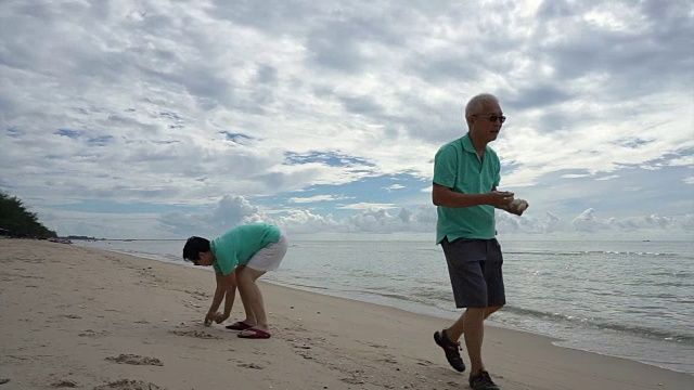 一对亚洲老夫妇在海滩上捡贝壳视频素材