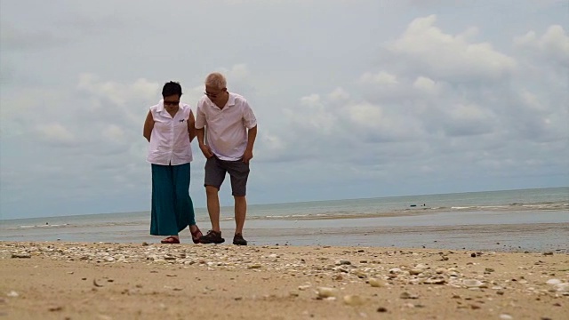 一对亚洲老夫妇在海滩上捡贝壳视频素材