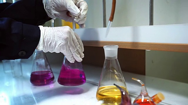 手在手套混合粉红色液体和黄色液体在flask实验室视频下载