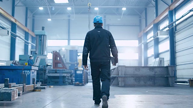 跟随镜头的工厂工人戴着安全帽走过工业设施。视频素材