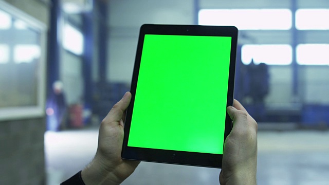 在工厂的工业环境中，一个带有绿色模拟屏幕的平板电脑的镜头。视频素材