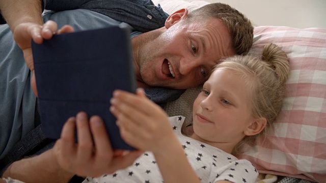 父亲和女儿躺在地板上使用数码平板电脑视频素材