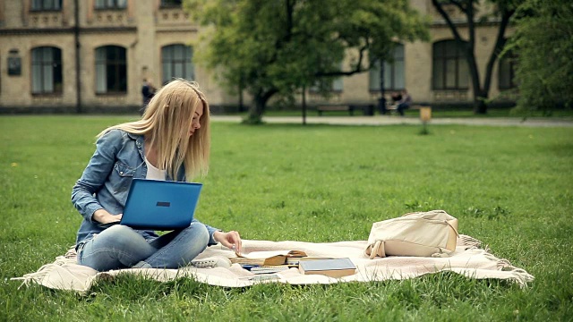 女学生坐在公园里用笔记本电脑。视频素材