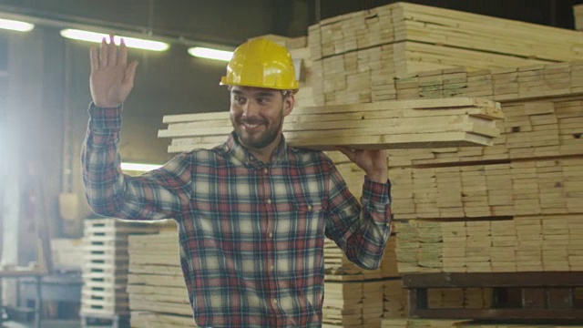 伐木场的工人戴着安全帽在仓库里搬运木材，同时问候同事。视频下载