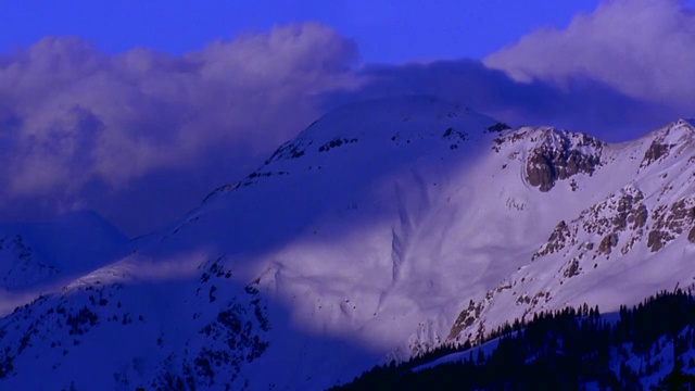 宽镜头延时滚动云后面的积雪覆盖的山与阴影/落基山脉，科罗拉多州视频素材