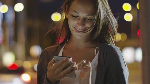 迷人的女人在夜间城镇的街道上使用手机视频素材