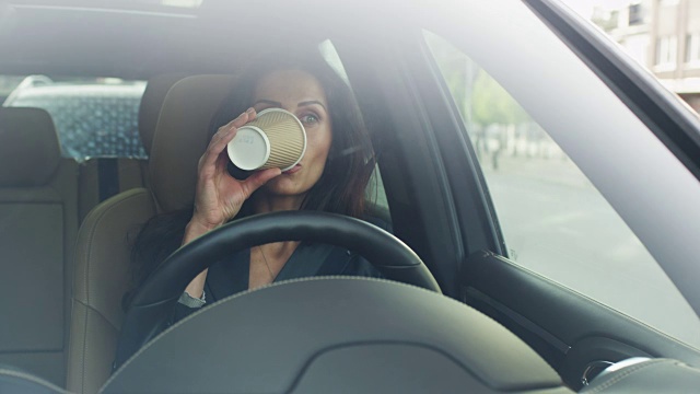 迷人的微笑商务女性在清晨开车。喝咖啡。视频素材