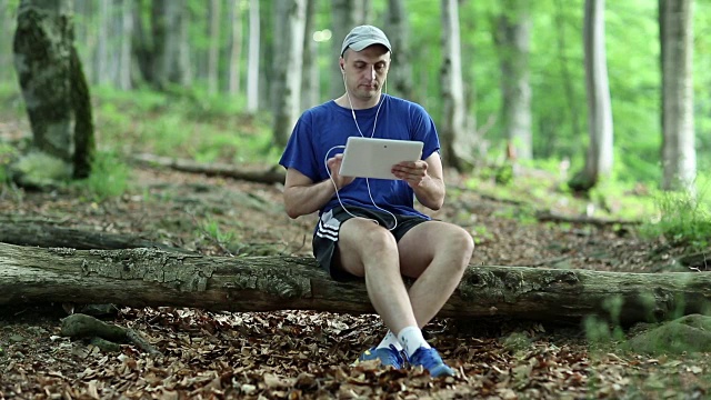 一个人拿着平板电脑坐在森林里的一根木头上视频素材