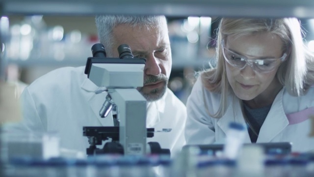男女科学家正在实验室里用显微镜和平板电脑工作。视频素材