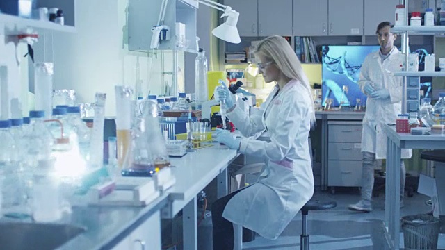 一名女科学家在实验室与同事一起工作时正在使用微型吸管。视频素材