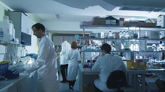 一队身穿白大褂的白种人科学家正在一个现代化的实验室里工作。视频素材