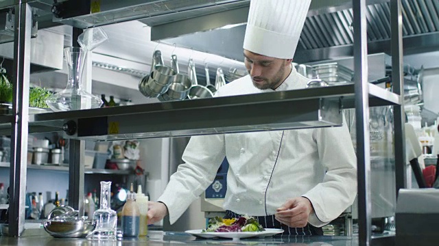 快乐的专业厨师在一个商业厨房装饰和提供沙拉。视频素材