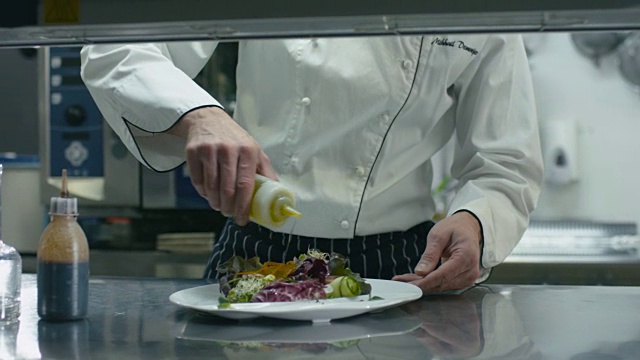 快乐的专业厨师在一个商业厨房装饰和提供沙拉。视频素材