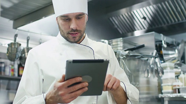 一家餐厅或酒店的商业厨房里的专业厨师正在使用平板电脑。视频素材