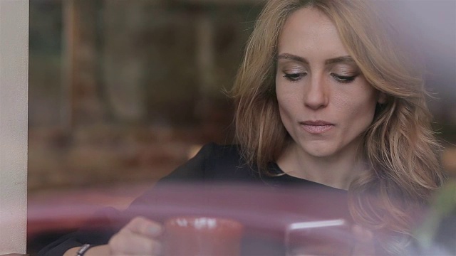 一名女子在咖啡馆用智能手机上的应用程序边喝咖啡边笑边发短信。视频素材