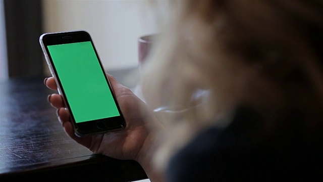 迷人的年轻女子使用她的绿色触摸屏手机在咖啡馆视频素材
