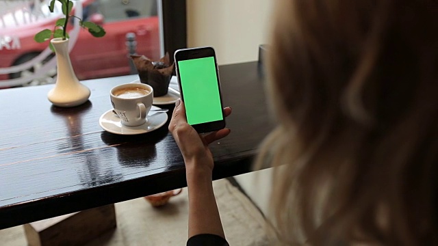 迷人的年轻女子使用她的绿色触摸屏手机在咖啡馆视频素材