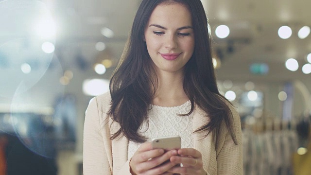 一个快乐的黑发女孩正站在一家百货商店里用智能手机发短信。视频素材