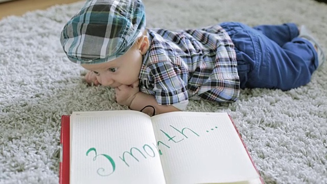 一个穿着格子衬衫，戴着格子帽的男婴正在看笔记本。视频下载