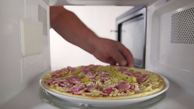 一名男子在家里的微波炉里给未煮过的火腿和奶酪披萨解冻视频下载