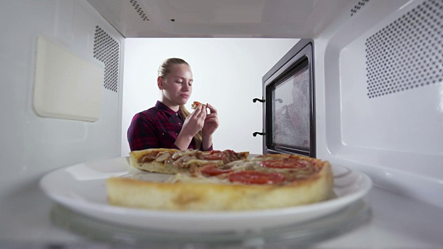 一个小女孩吃了一片刚在微波炉里加热过的披萨视频素材