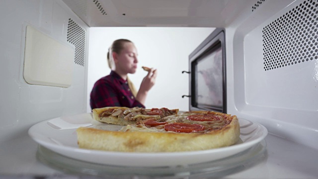 女孩用微波炉加热食物，烤披萨放在烤箱里的盘子里视频下载