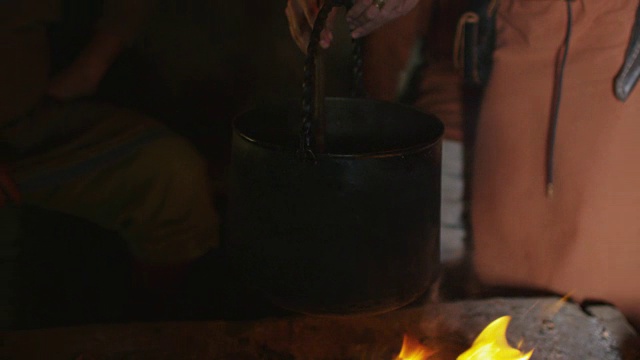 穿着中世纪服装的女人在火上做饭。中世纪的产物。视频素材