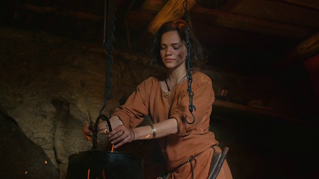 穿着中世纪服装的女人在火上做饭。村民的生活。中世纪的产物。视频素材