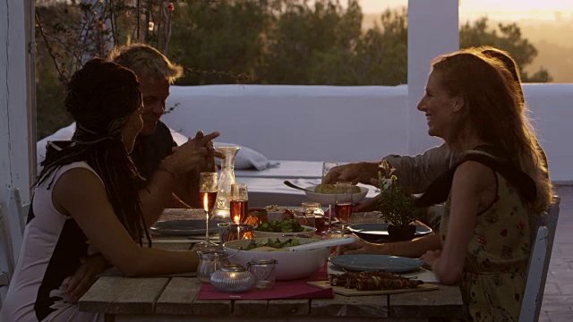 两对夫妇在屋顶露台的餐桌上吃晚餐，这是用R3D拍摄的视频素材