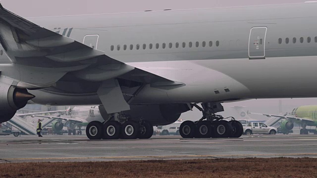 一架波音777 300ER的轮子和涡轮机在机场的跑道上移动。近景，大雾天气视频下载