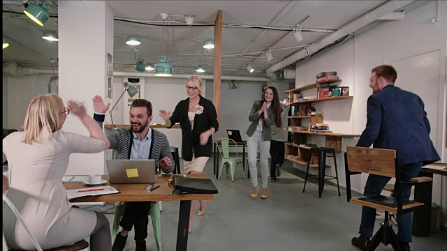 一个在笔记本电脑上工作的人发现了好消息，每个人都高兴地祝贺和鼓掌他的商业团队在启动办公室视频下载