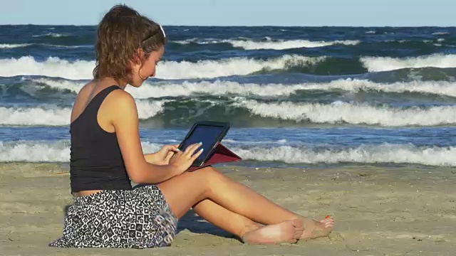 年轻女性大笑，而有有趣的聊天会议上她的平板电脑在海滩上视频素材