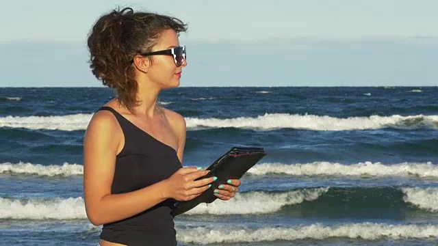 美丽的女孩在海边玩她的平板电脑视频素材