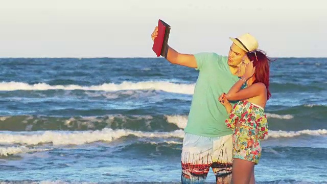 一对美丽的夫妇在海边用平板电脑视频通话，与朋友保持联系视频素材