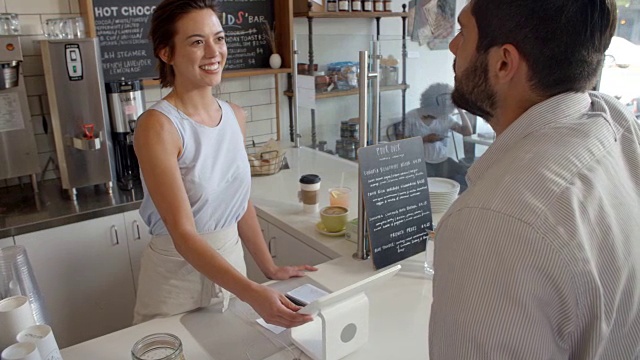 一个顾客在咖啡店用卡付给微笑的女服务员视频素材