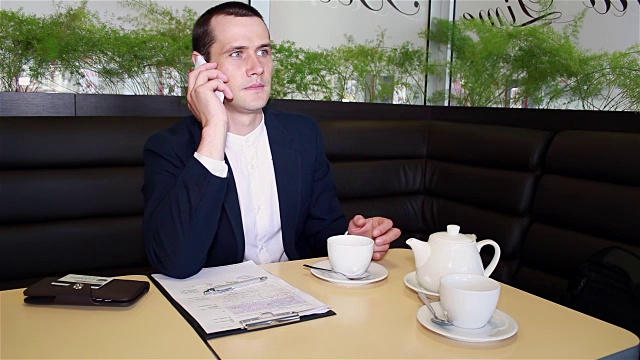 商人坐在咖啡馆里喝着咖啡，讲着电话视频素材