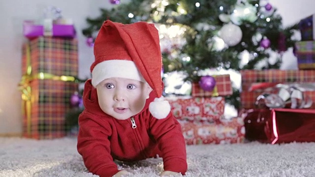 穿着圣诞老人服装的小男孩爬到圣诞树旁。视频下载