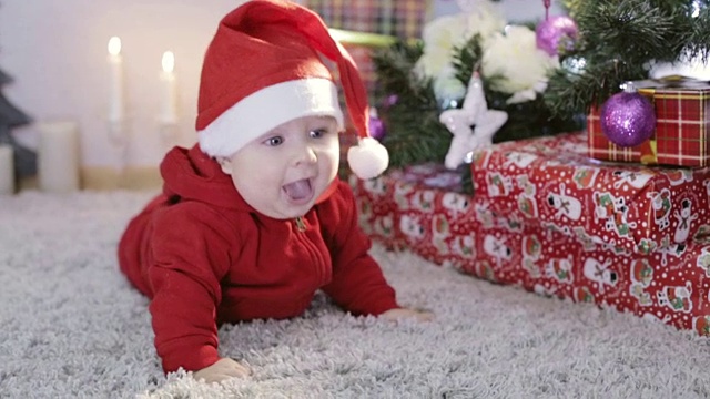 穿着红色圣诞老人服装的有趣的小孩在圣诞树上玩玩具，微笑着。视频下载