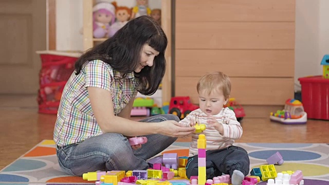 可爱的小男孩和妈妈在家里玩玩具积木，在房间的地板上坐着。视频素材