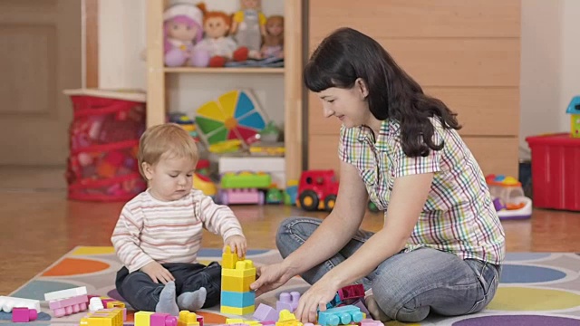 可爱的小男孩和妈妈在家里玩玩具积木，在房间的地板上坐着。视频素材