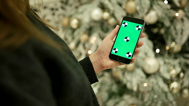 女性手触摸手机绿色屏幕的特写。色度键。关闭了。跟踪运动。垂直的。与模糊的圣诞装饰背景视频下载