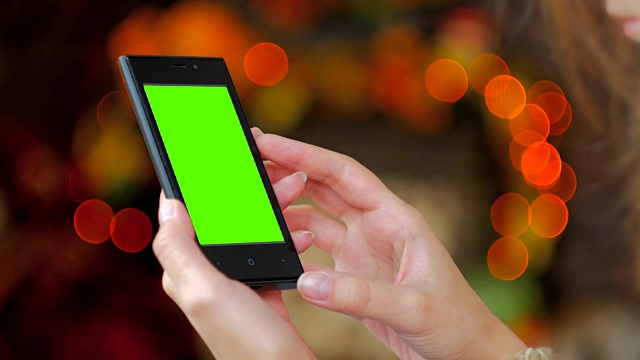一个女人在看绿色屏幕的智能手机视频下载