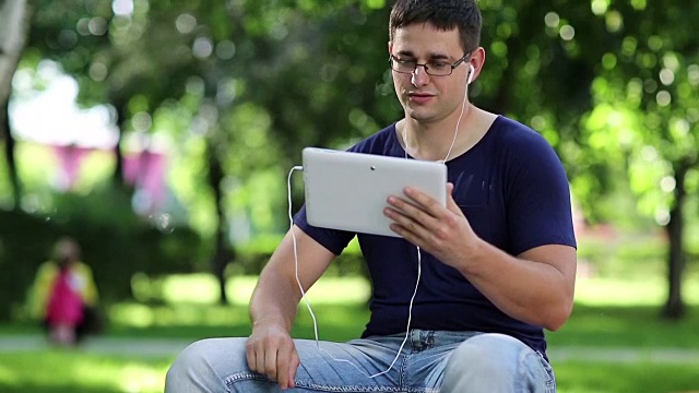 一名男子坐在城市公园的长椅上，通过平板电脑交流视频素材