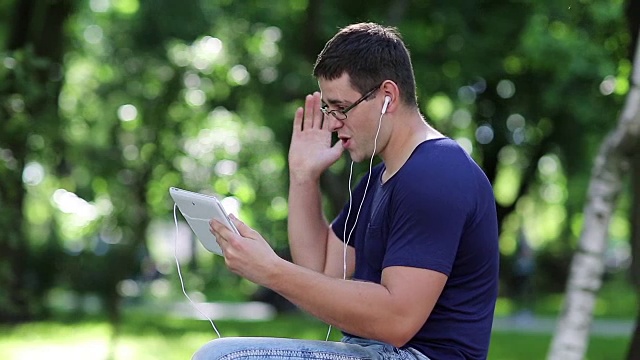 一名男子坐在城市公园的长椅上，通过平板电脑交流视频素材